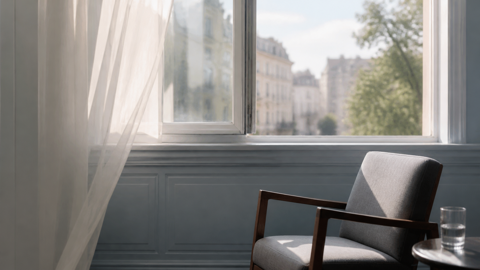 An empty chair beside an open window, with a glass of water on a small table.
